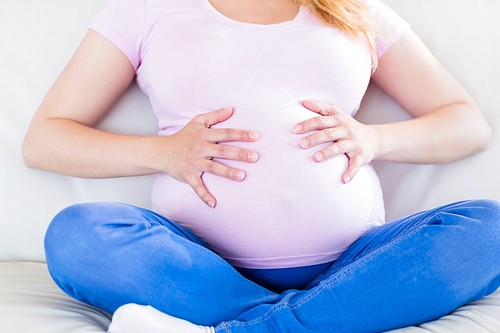 Close up of pregnant woman sitting on couch touching her belly in the living room