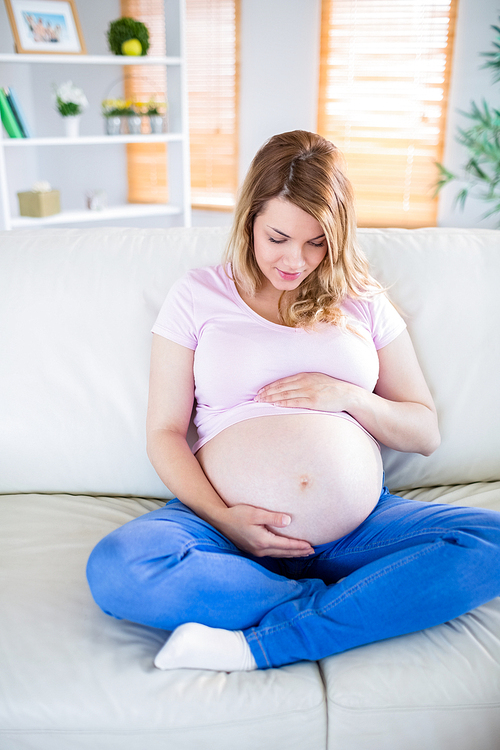 Pregnant woman sitting on couch touching her belly at home in the living room
