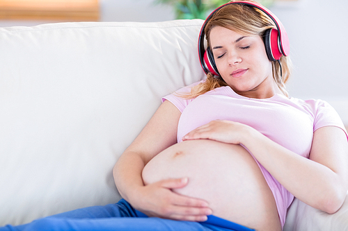Pregnant woman listening music and touching her belly at home in the living room