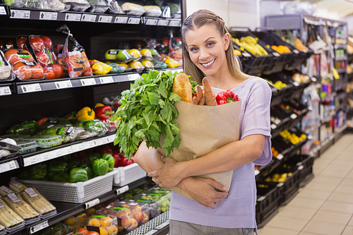 Pretty blonde holding bag with bread and vegetable in supermarket