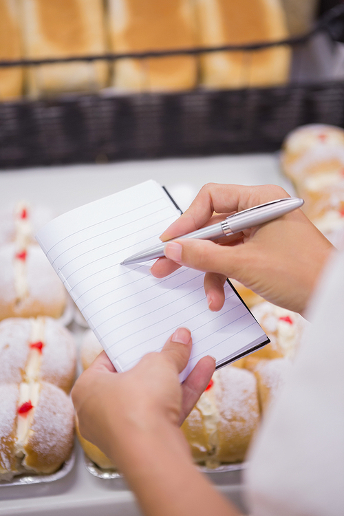 a woman  taking notes above pastries in a supermarket