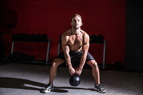 Squat muscular man lifting a kettlebell at the crossfit gym