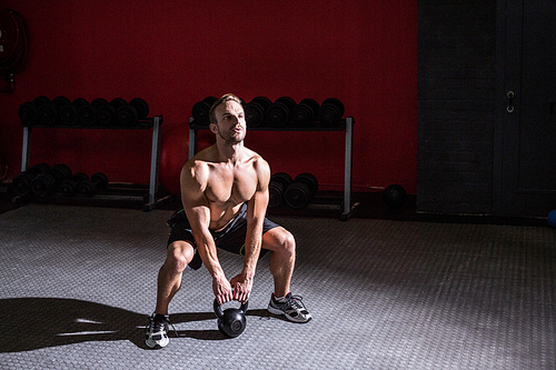 Squat muscular man lifting a kettlebell at the crossfit gym