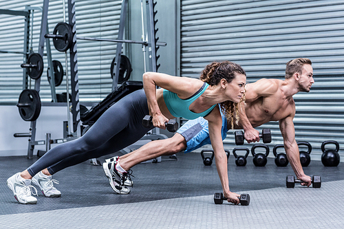 Muscular couple doing plank exercise while lifting weights