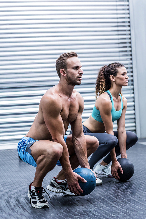 Squatting muscular couple doing ball exercise