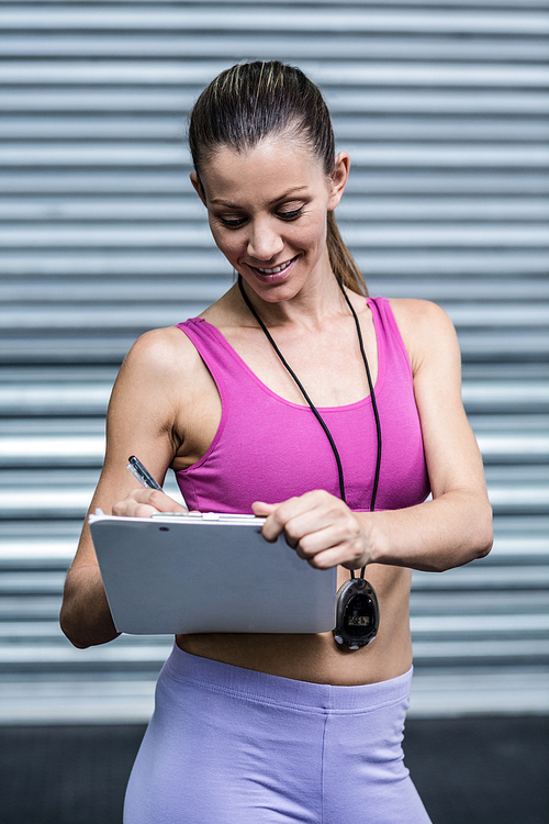 Smiling female coach writing on her notepad at the crossfit gym