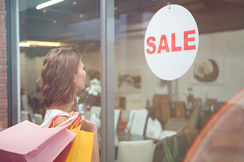 Smiling woman with shopping bags looking at window at the shopping mall