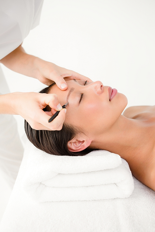 Woman using tweezers on patient eyebrow at the health spa