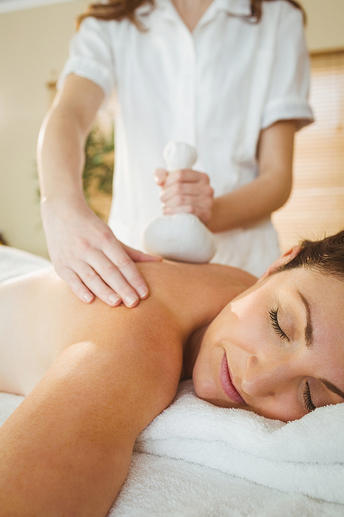 Young woman getting herbal compress massage in therapy room