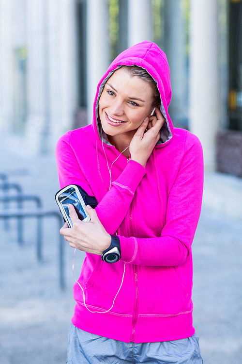 A woman wearing a pink jacket putting her headphones on a sunny day