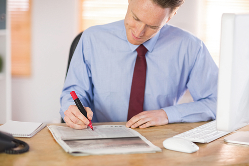 Businessman marking the newspaper with marker in his office