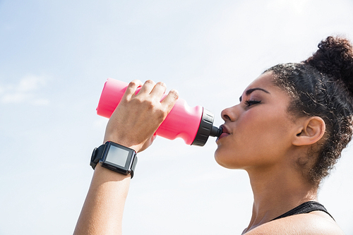 Fit woman wearing smart watch and drinking at the beach