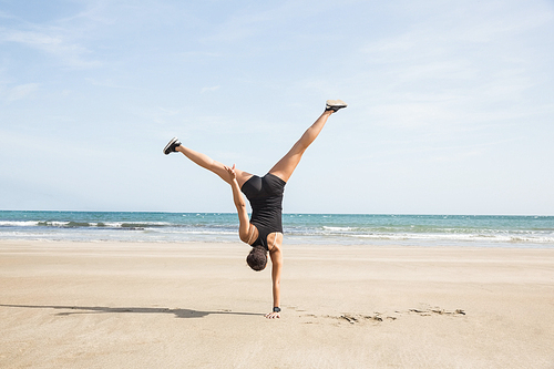 Fit woman cartwheeling on the sand at the beach