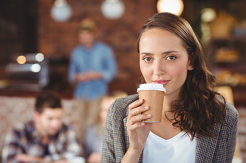 Portrait of smiling young woman drinking from take-away cup at coffee shop