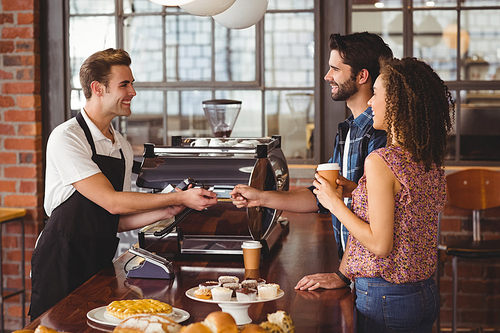 Smiling hipster giving credit card to barista at coffee shop