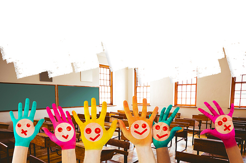Hands with colourful smiley faces against empty classroom