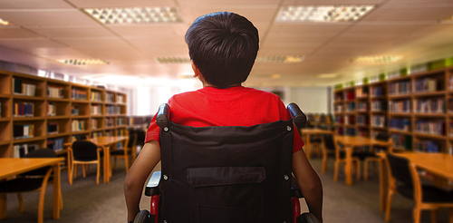Rear view of boy sitting in wheelchair against view of library