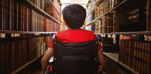 Rear view of boy sitting in wheelchair against close up of a bookshelf