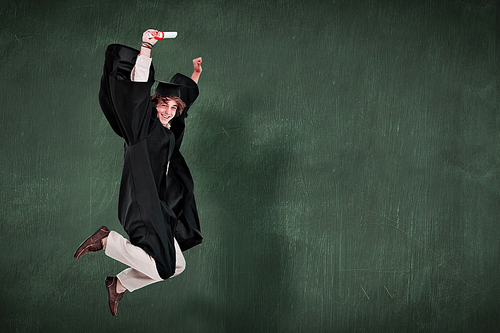 Happy male student in graduate robe jumping against green chalkboard