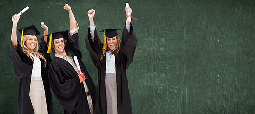 Three students in graduate robe raising their arms against green chalkboard