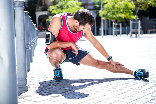 Handsome athlete doing leg stretching on the floor on a sunny day