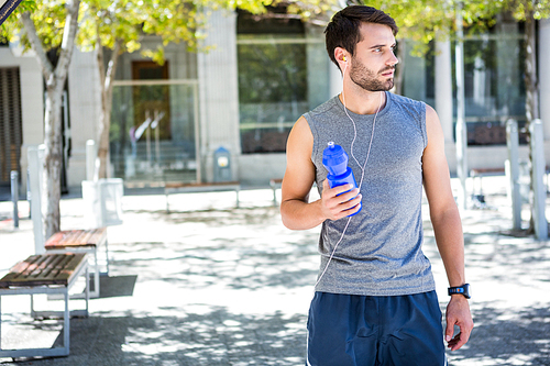 Handsome runner holding a water bottle on a sunny day