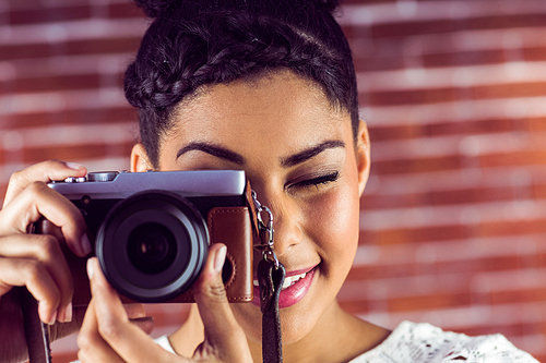 Young hipster taking a picture against a brick wall