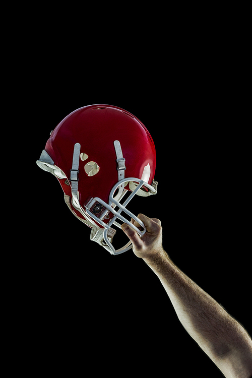 American football player holding up his helmet against black background