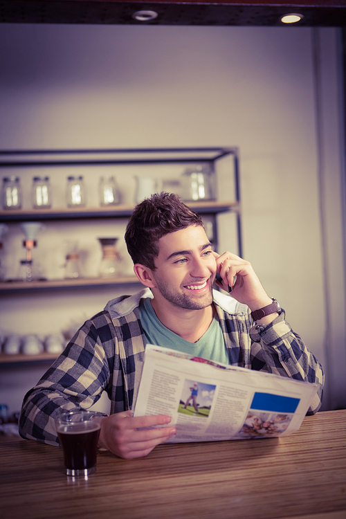 Smiling hipster phoning and holding newspaper at coffee shop