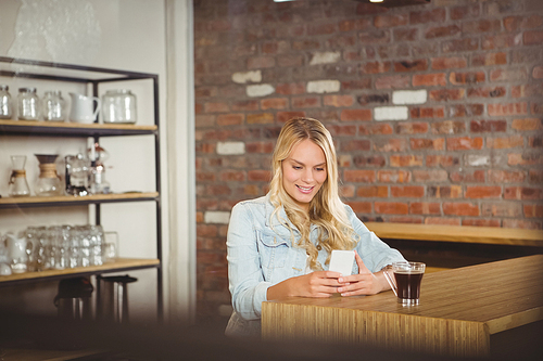 Smiling blonde having coffee and using smartphone at coffee shop