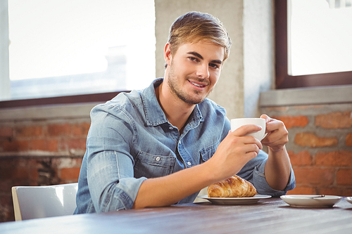 Portrait of handsome man enjoying coffee and croissant at coffee shop