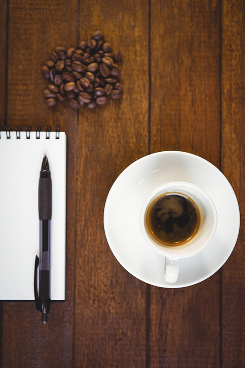 Cup of coffee and notepad with pen on wooden table