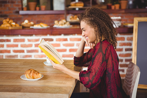 Young happy woman reading a book in a cafe