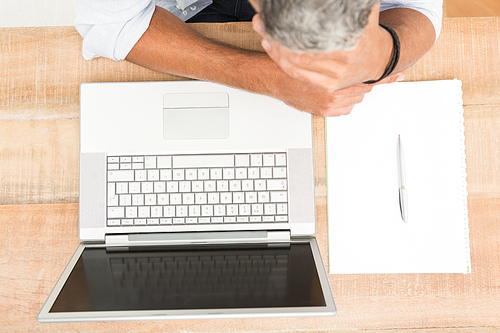 Exhausted casual businessman leaning on wooden desk next to laptop