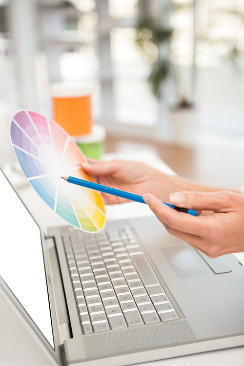 Casual designer working with laptop and colour chart in the office