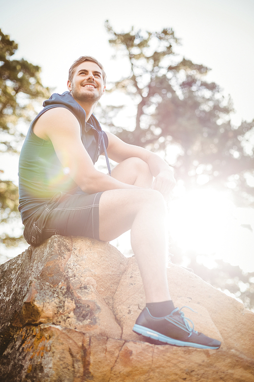 Young happy jogger sitting on rock and looking away in the nature