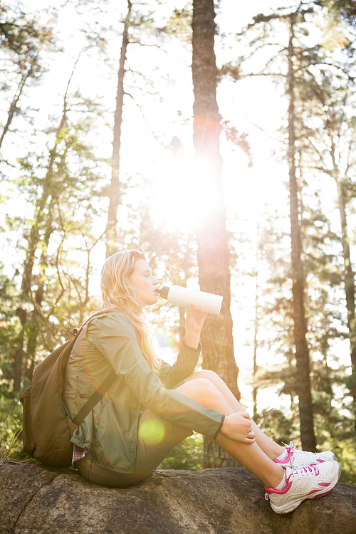 Pretty blonde hiker drinking and sitting on stone in the nature