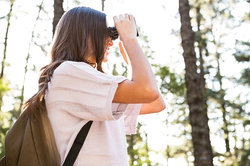 Smiling brunette hiker looking through binoculars in the nature