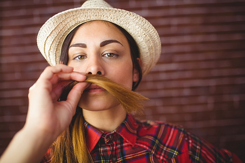 Beautiful hipster holding hair as mustache on red brick background