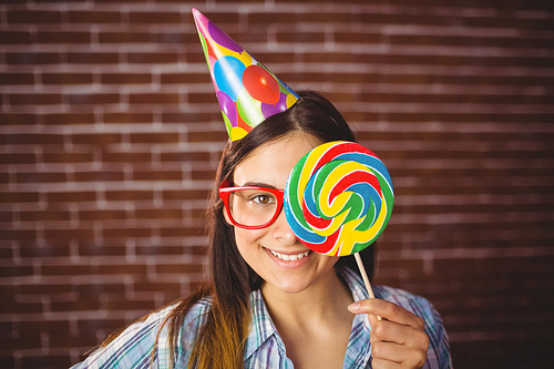 Pretty hipster with party hat and lollipop on red brick background