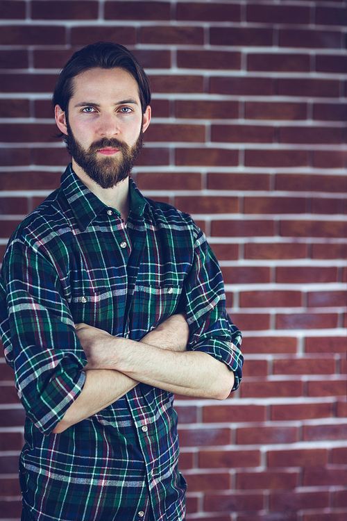 Portrait of confident hipster with arms crossed stading against brick wall