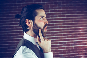 Side view of hipster with hand on chin thinking against brick wall