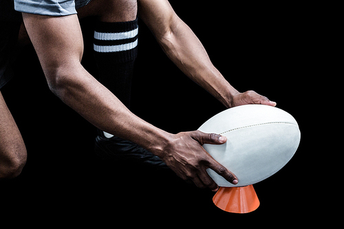 Cropped image of sportsman keeping rugby ball on kicking tee against black background