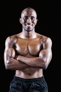 Portrait of happy shirtless athlete standing with arms crossed on black background