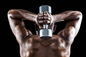 Rear view of muscular man lifting dumbbell behind head against black background