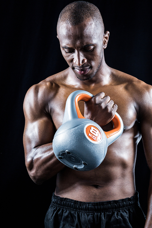 Muscular man exercising with kettlebell against black background