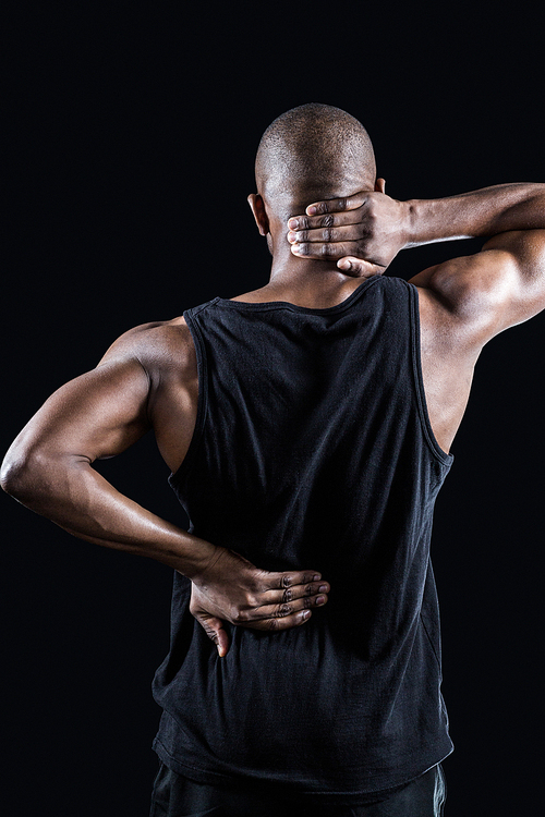 Rear view of muscular man suffering from backache while standing against black background