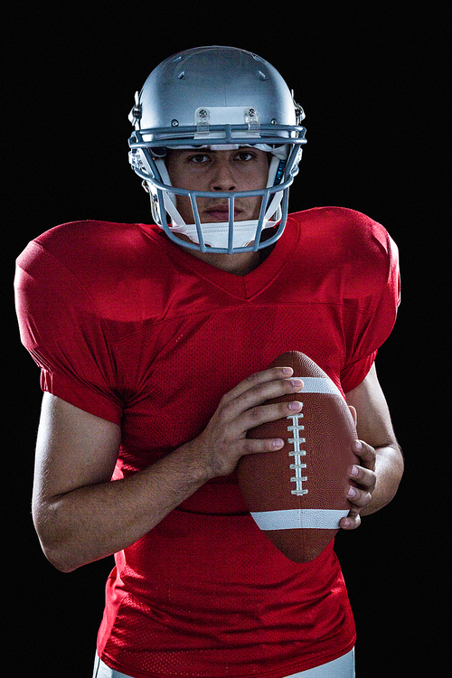 Portrait of confident sportsman with American football standing against black background