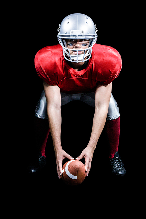 American football player bending while holding ball against black background