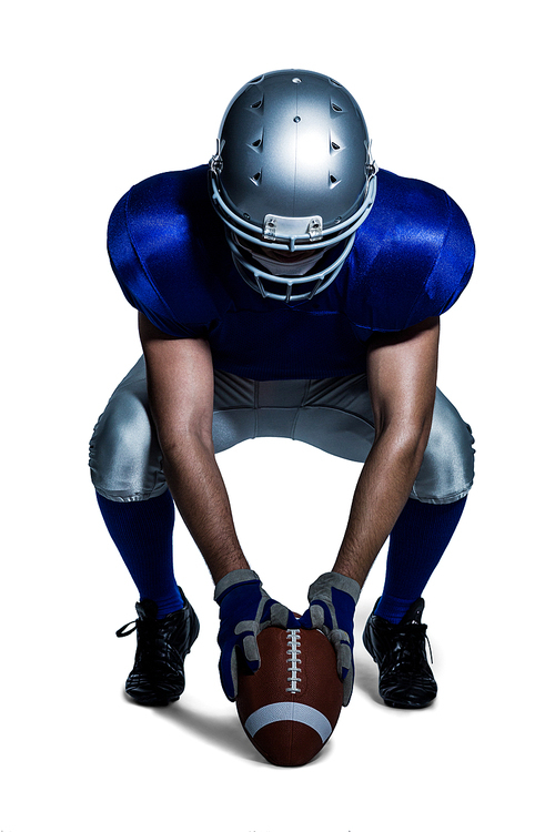 American football player in uniform holding ball while crouching against white background